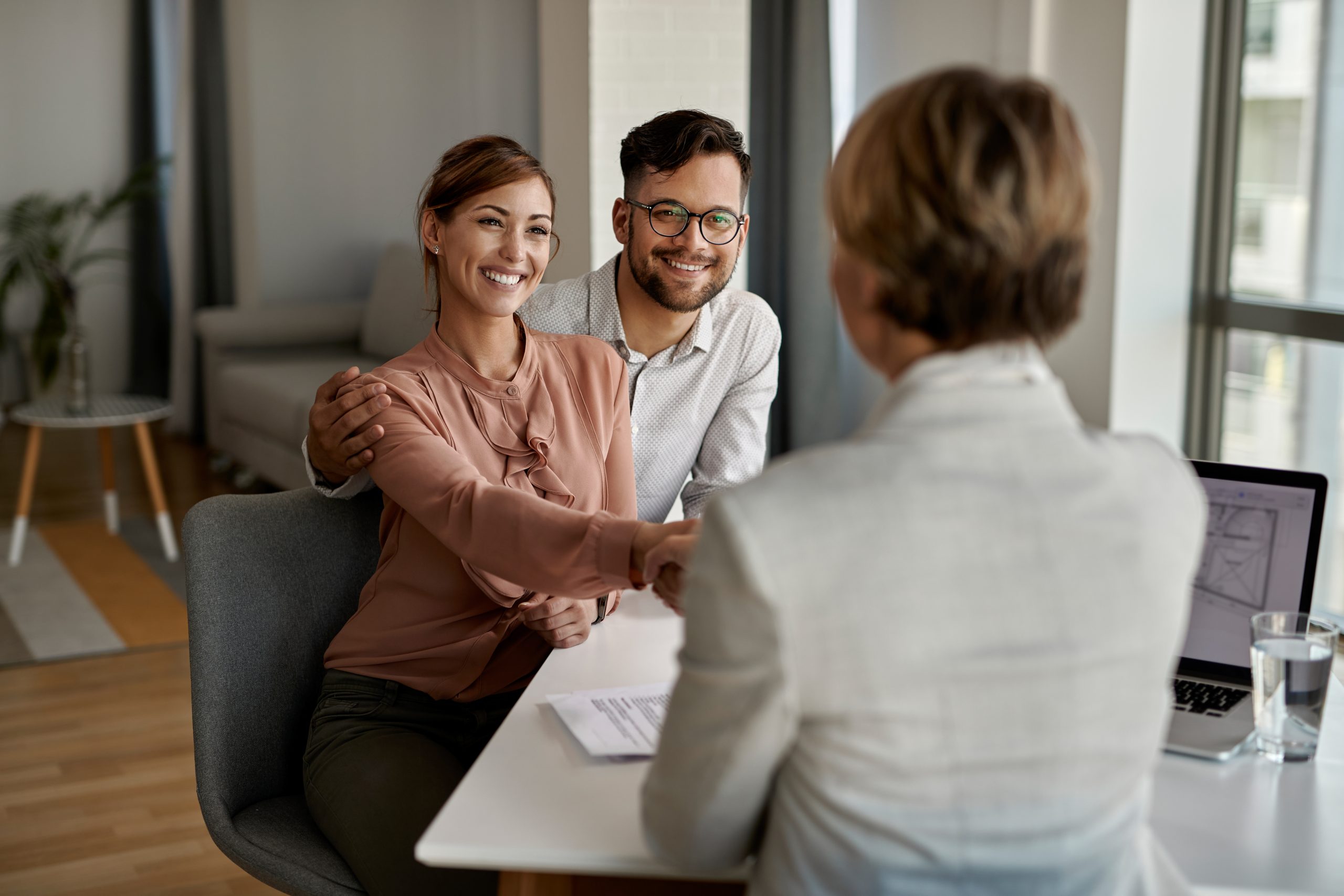 Young happy couple shaking hands with insurance agent during a meeting in the office.